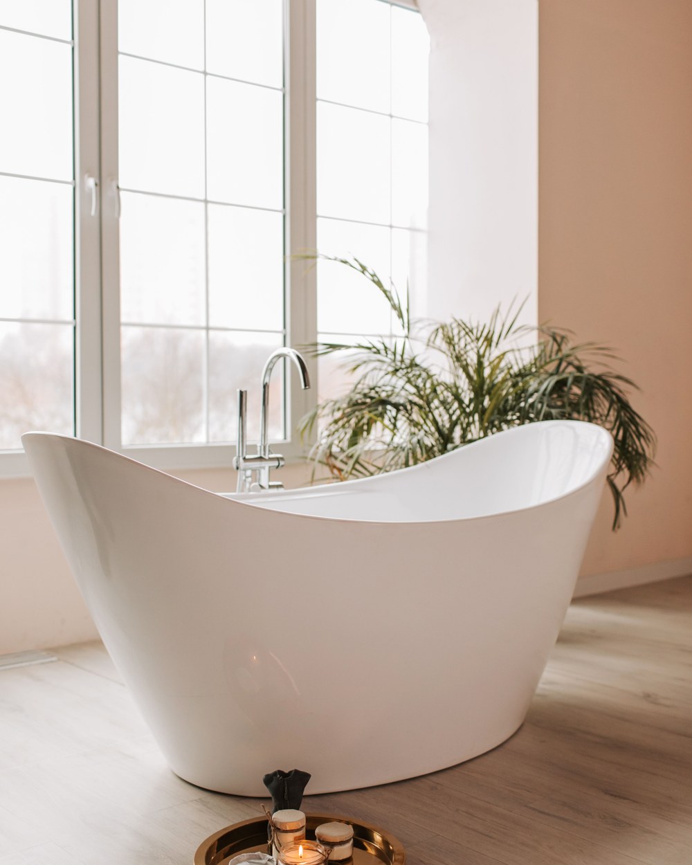 Coastal Bathroom Ideas: Small Bathroom Before and After 4 Bright bathroom with a white freestanding bathtub, a palm plant and a rattan tray with candles in warm natural light